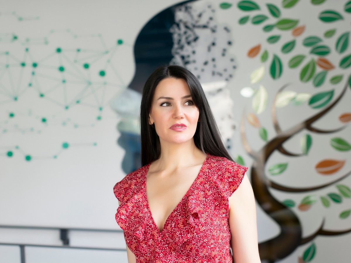 A woman in a red dress and brown hair looks off to the side of the camera. She is Nuritas founder Dr Nora Khaldi.