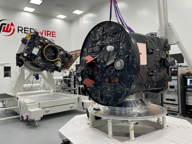 Two spacecrafts in a cleanroom. The Redwire logo is on the wall in the background.