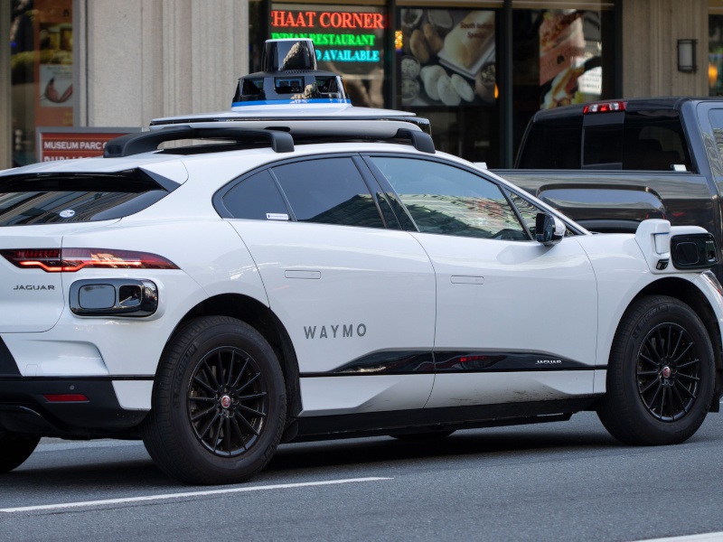 A white Jaguar car belonging to Waymo’s robotaxi fleet, seen here on a city street. The company is owned by Alphabet.