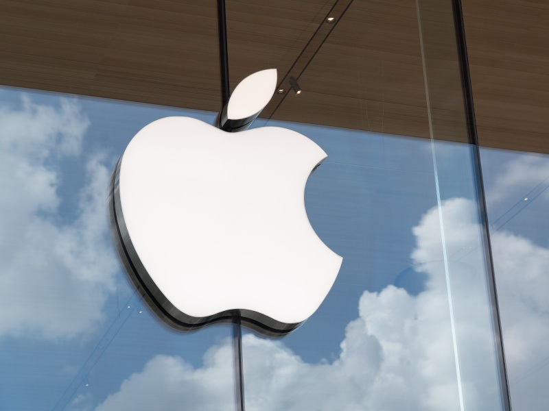 An Apple logo on a glass building, with the sky reflected on the surface.