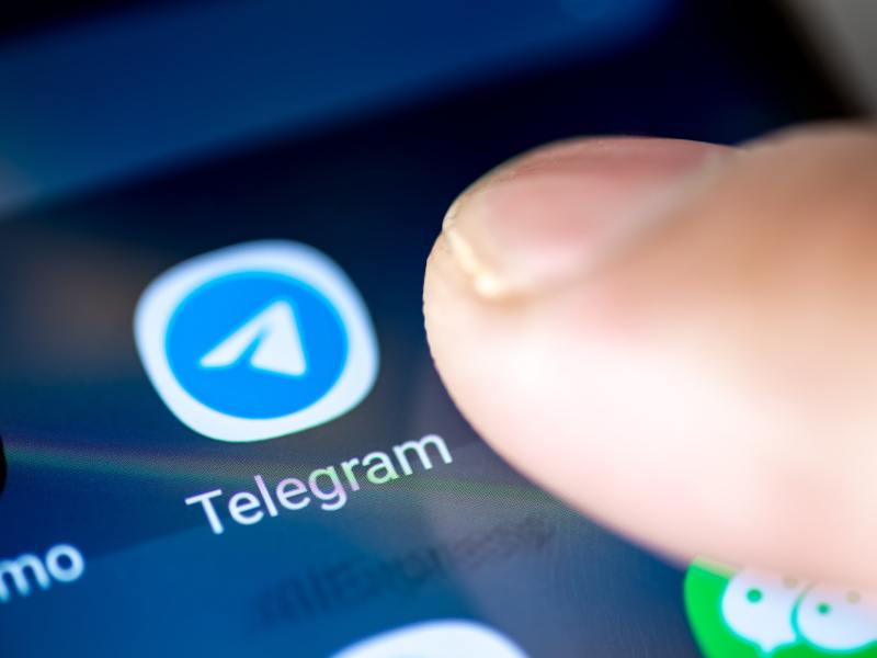 A person's finger touching the Telegram app icon on a smartphone.