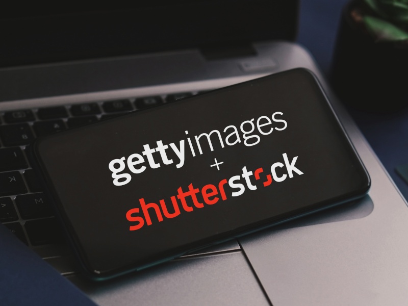 A phone resting on a laptop. The official logos for Getty Images and Shutterstock are displayed on the phone’s screen.