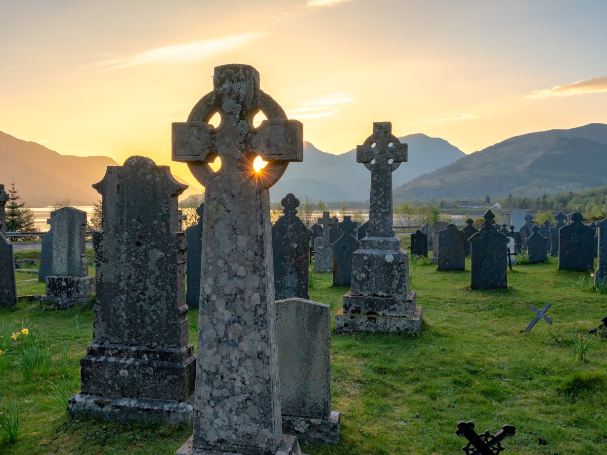 A graveyard at sunrise with a Celtic-style grave in the foreground.