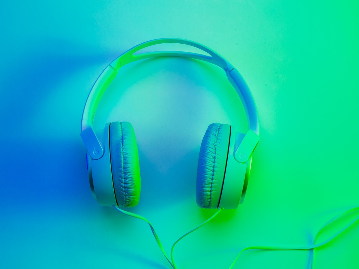 A pair of bright headphones on a vibrant green-blue background.