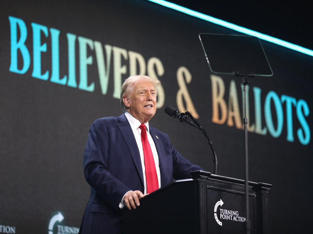 Trump stands on a podium in front of a sign that says 'believers and ballots'.